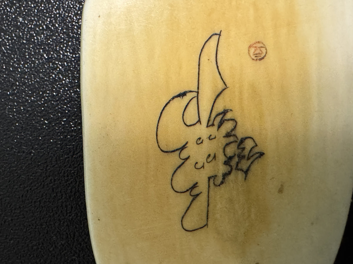 Carved ox horn pendant with Chinese calligraphy inscribed vertically, shown against textured surface with penny placed upper right for scale reference.