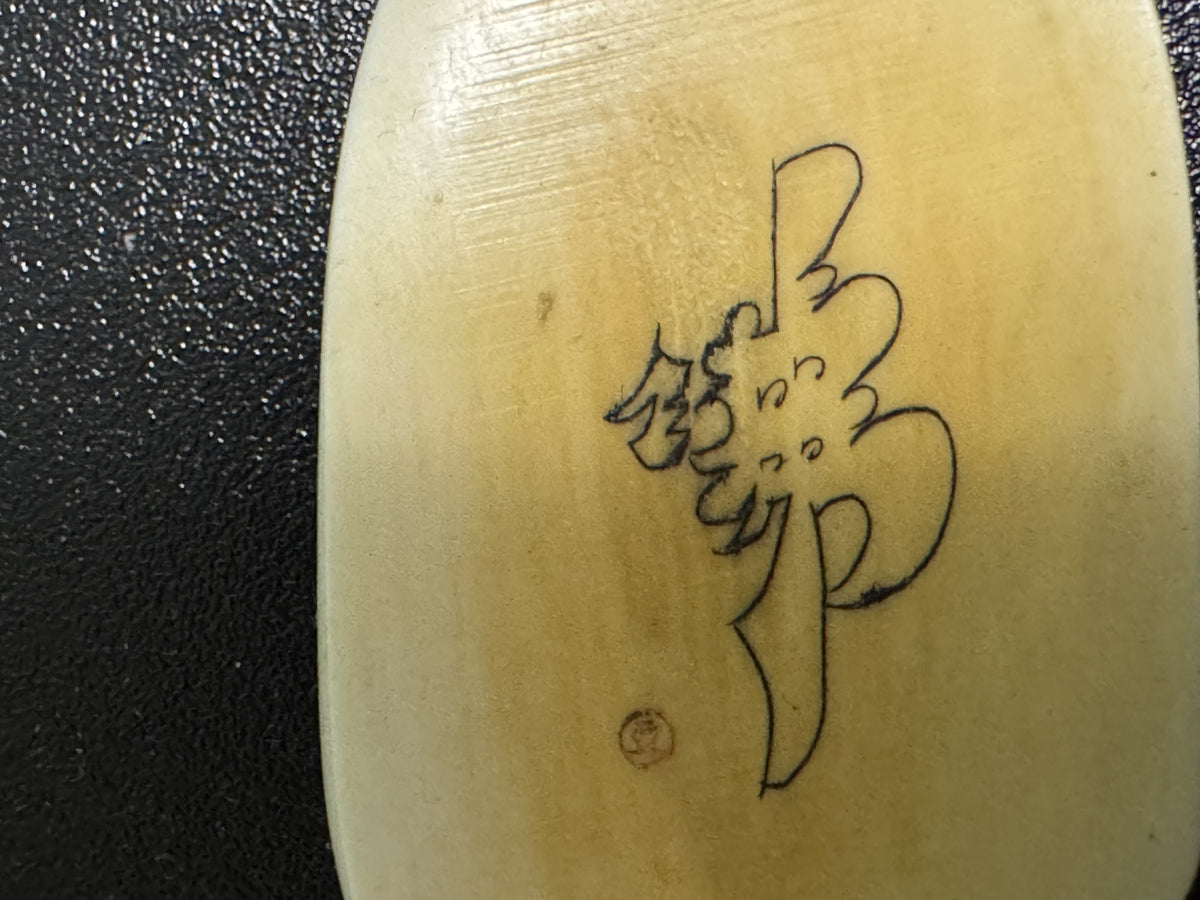 Cream-colored ox horn pendant carved with Chinese characters and decorative motifs, photographed against dark textured surface, showing front face with inscribed text and ornamental design.