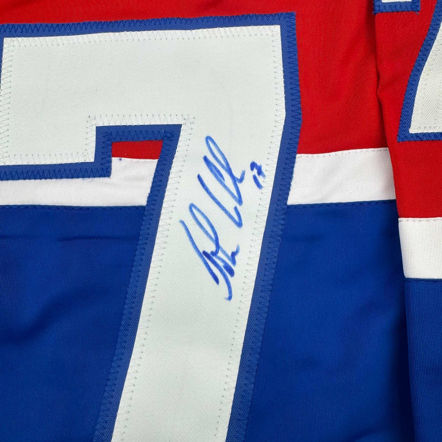Close-up of blue and white striped jersey sleeve with blue handwritten signature on white nameplate strip.