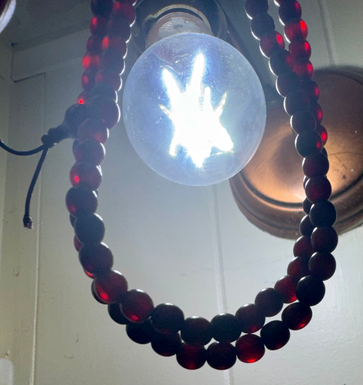 The horn bead necklace hung in front of a light bulb, the beads glowing translucent red with the light behind them