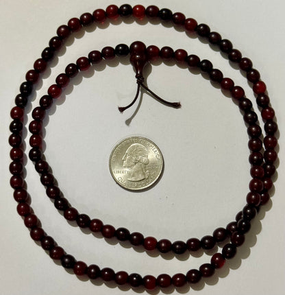 The horn bead strand coiled in two loops around a US quarter for scale, the head bead and two cord tails at the top