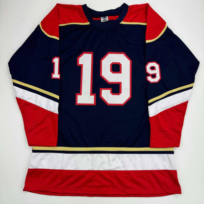 Navy blue hockey jersey with red and gold trim displaying number 19 in white and red stitching, laid flat against white background.