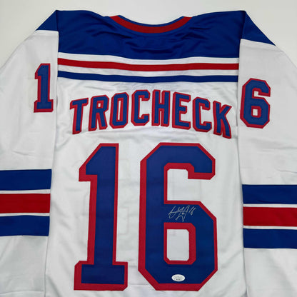 White hockey jersey with navy and red striping, displaying "TROCHECK" and number 16 on back, with visible autograph.