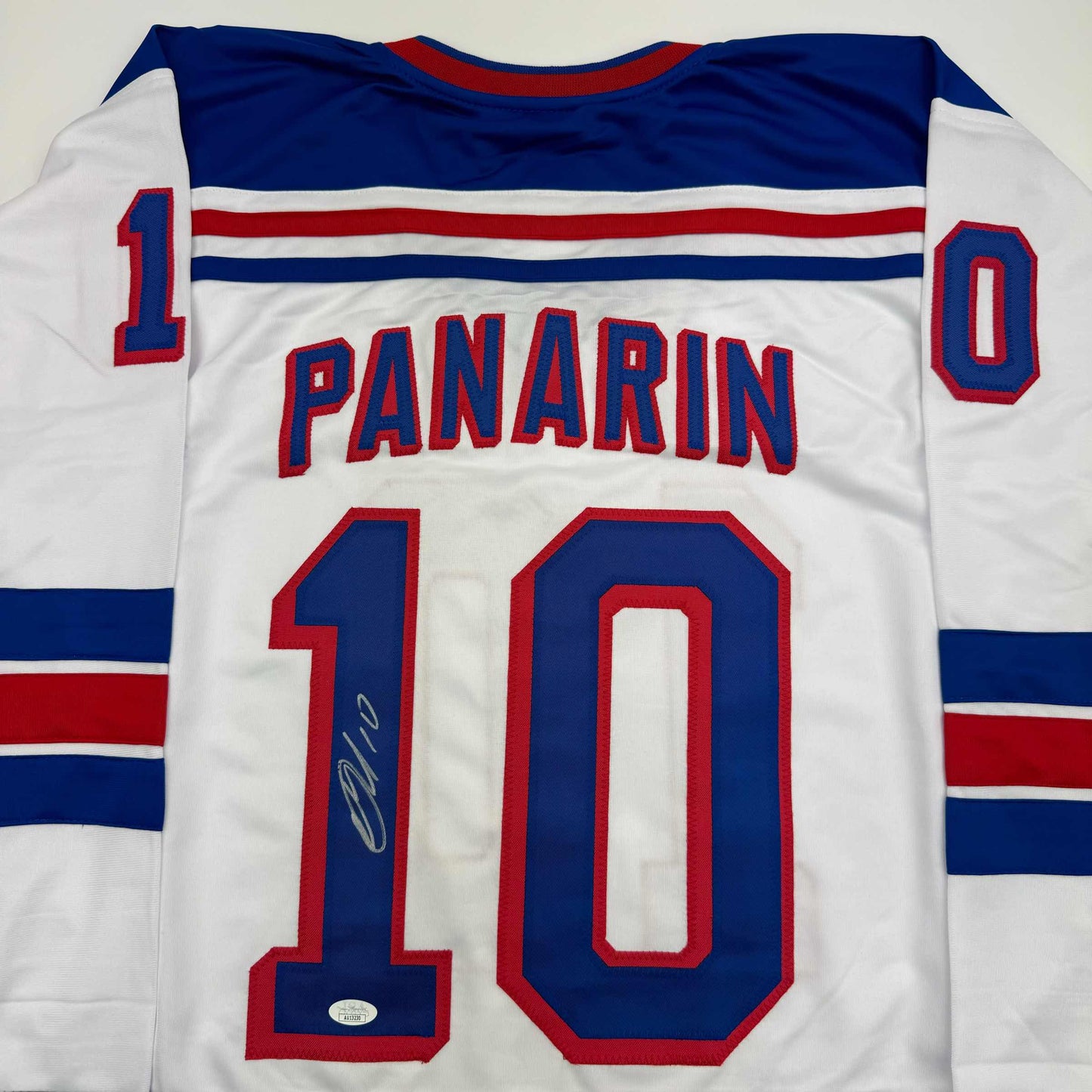 Back view of white hockey jersey with navy and red stripes, displaying "PANARIN" and number "10" in navy and red lettering, with autographed signature visible on the number.