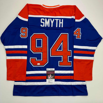 Blue Edmonton Oilers hockey jersey with red and white stripes, displaying "SMYTH" and number 94, with JSA authentication certificate visible at bottom center.