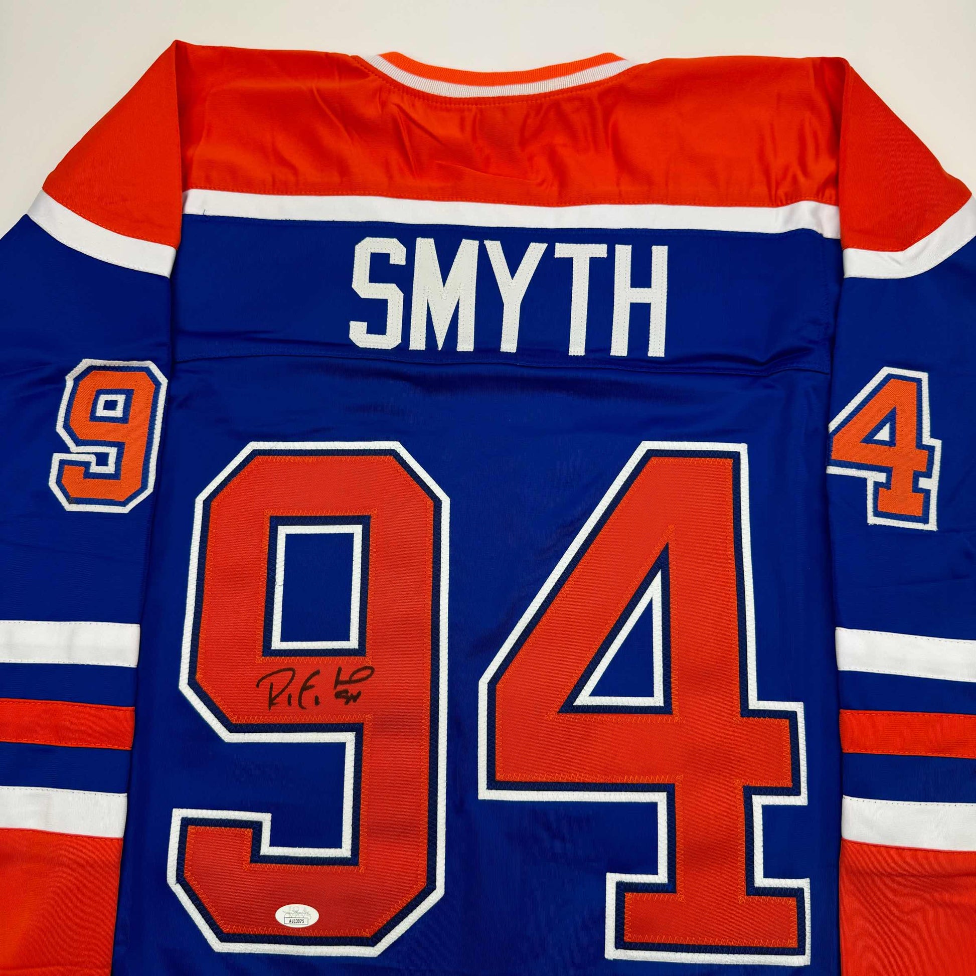 Back view of blue Edmonton Oilers hockey jersey with "SMYTH" nameplate and autographed number 94 in red and white.