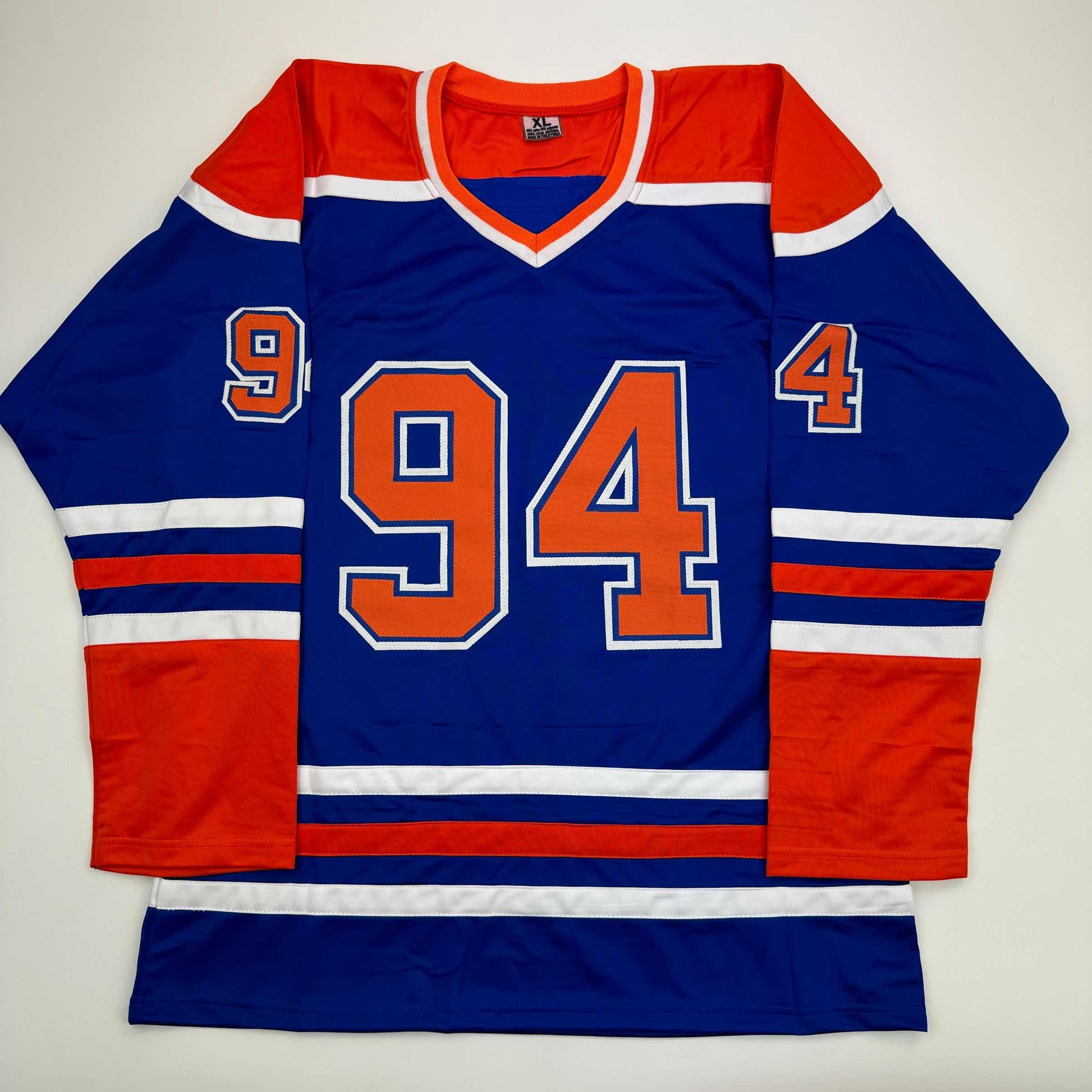 Flat lay of blue Edmonton Oilers hockey jersey number 94 with red and white stripes and orange numerals.