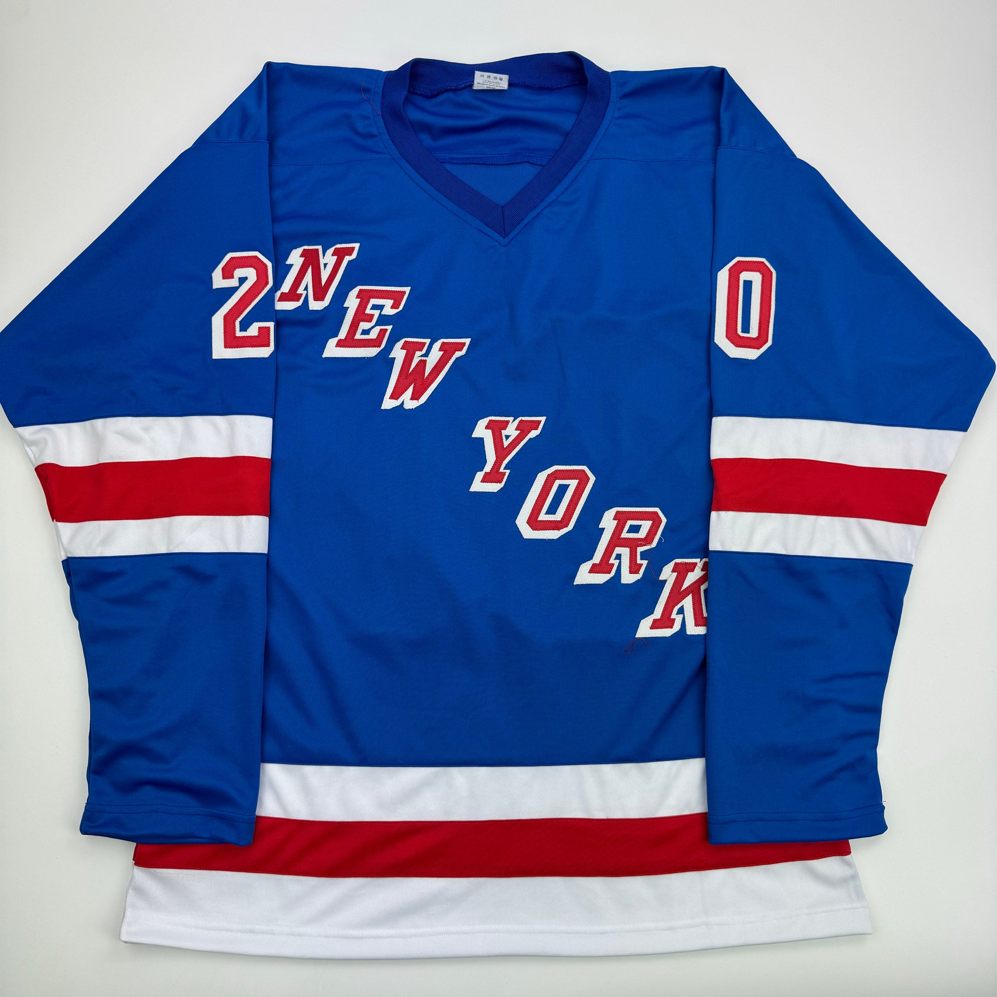 Blue New York Rangers hockey jersey with red and white striped sleeves, displaying "2NEW YORK" and "0" text, laid flat on white background.