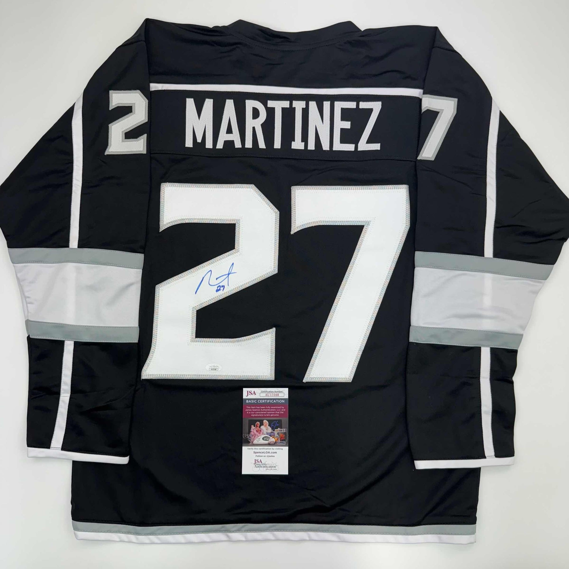 Back view of black LA Kings hockey jersey number 27 with white "MARTINEZ" nameplate and signature, displayed flat with JSA authentication certificate visible at bottom.