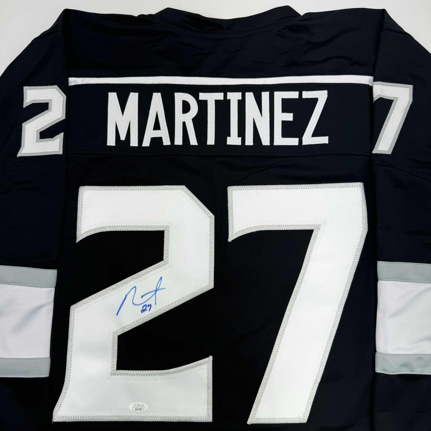 Back view of black hockey jersey displaying "MARTINEZ 27" with white stitched numbers and a blue autograph on the number seven.