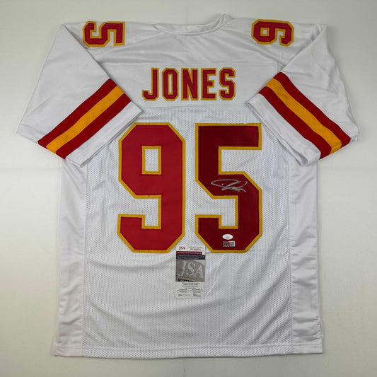 White Kansas City Chiefs football jersey number 95 with red and gold lettering, signed by Chris Jones, displayed flat with JSA authentication certificate visible.