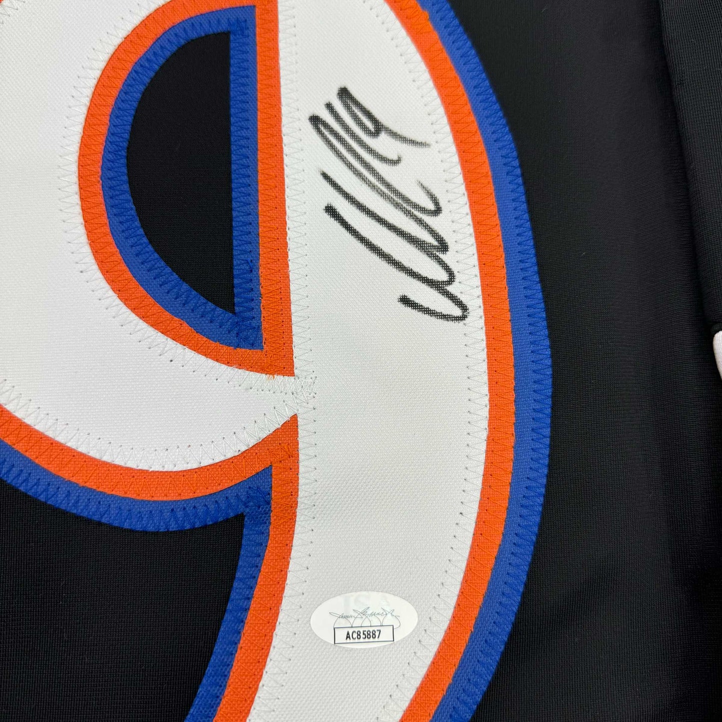Close-up of signed hockey jersey showing autographed blue and orange striped panel with authentication hologram sticker.