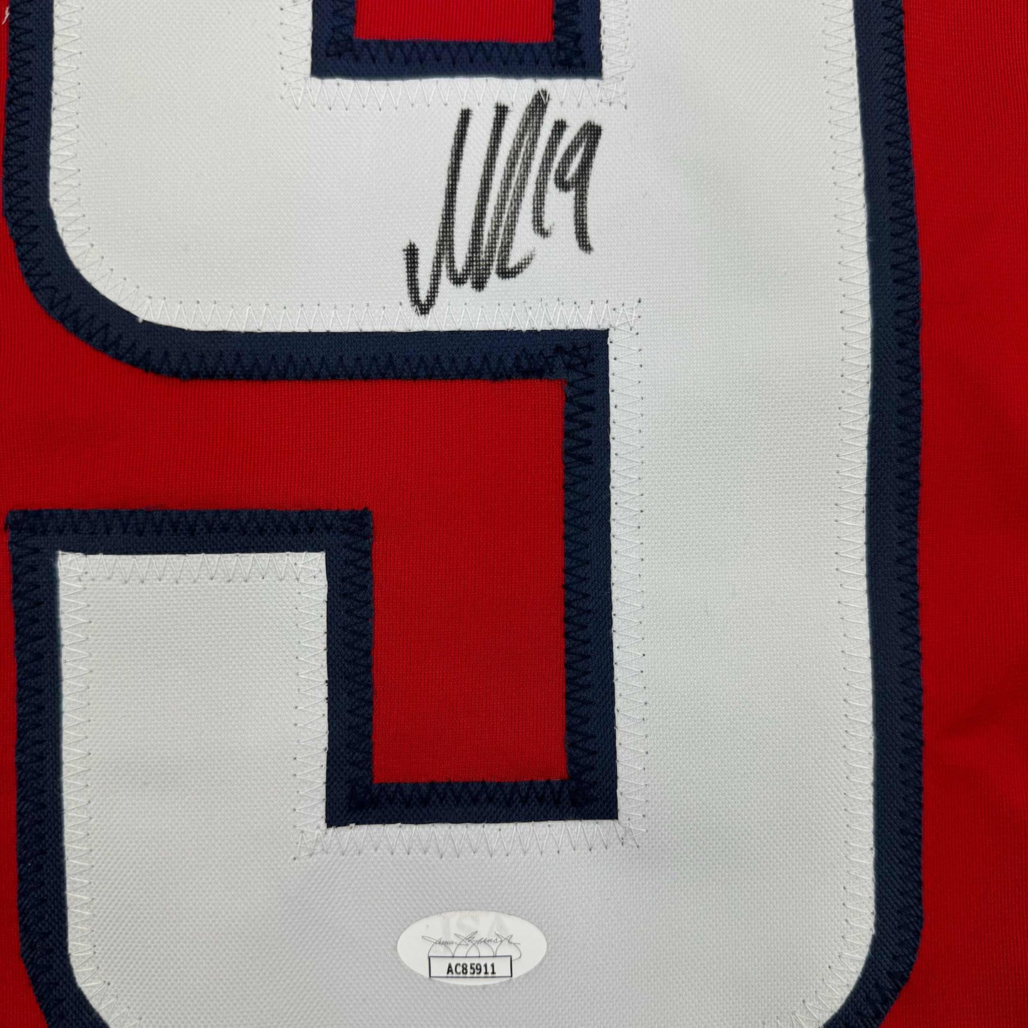 Close-up of signed red, white, and navy hockey jersey showing autographed area and JSA authentication sticker.