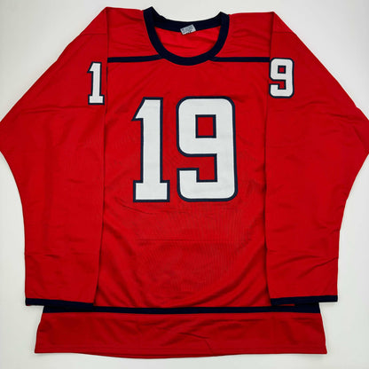 Red hockey jersey with white and navy number 19 displayed flat against white background, front view.