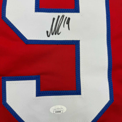 Close-up of autographed red, white, and blue hockey jersey front showing handwritten signature and JSA authentication sticker.