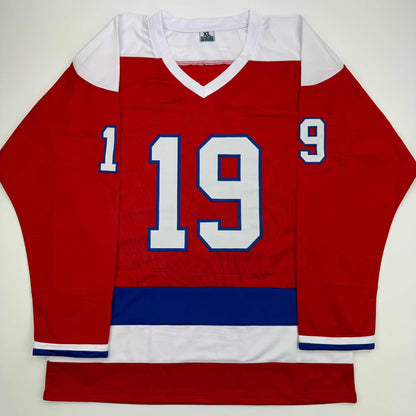 Red hockey jersey with white shoulders and collar, displaying large white and blue number 19, laid flat on white background.