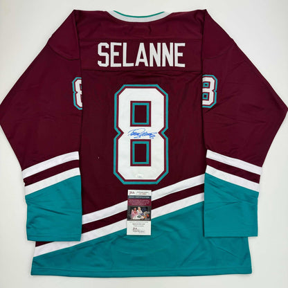 Flat lay of maroon and teal hockey jersey with "SELANNE" and number 8 on back, displaying JSA authentication certificate.