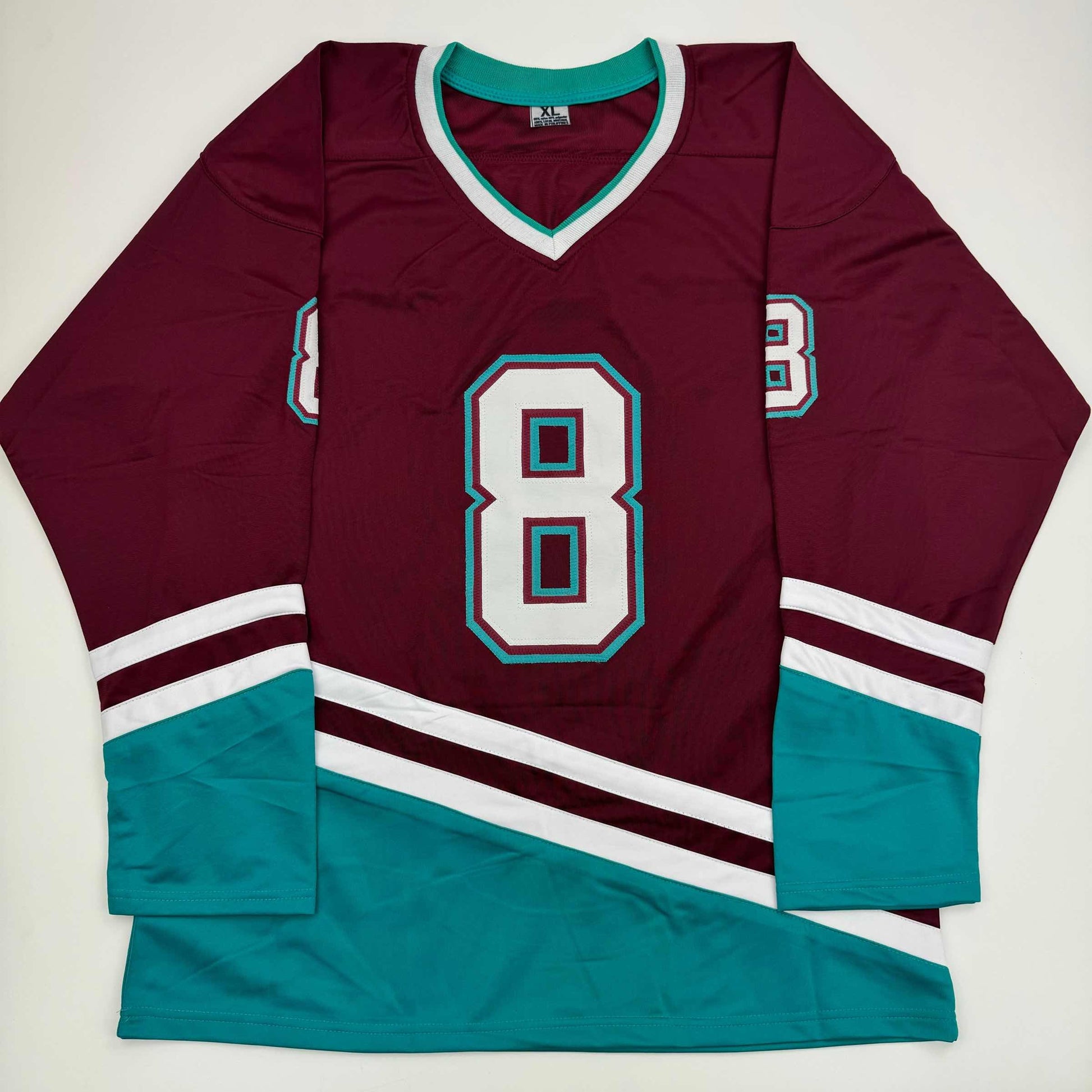 Flat lay of maroon and teal hockey jersey with number 8, white and teal trim on sleeves and collar.