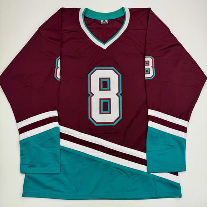 Flat lay of maroon and teal hockey jersey with number 8, white and teal trim on sleeves and collar.
