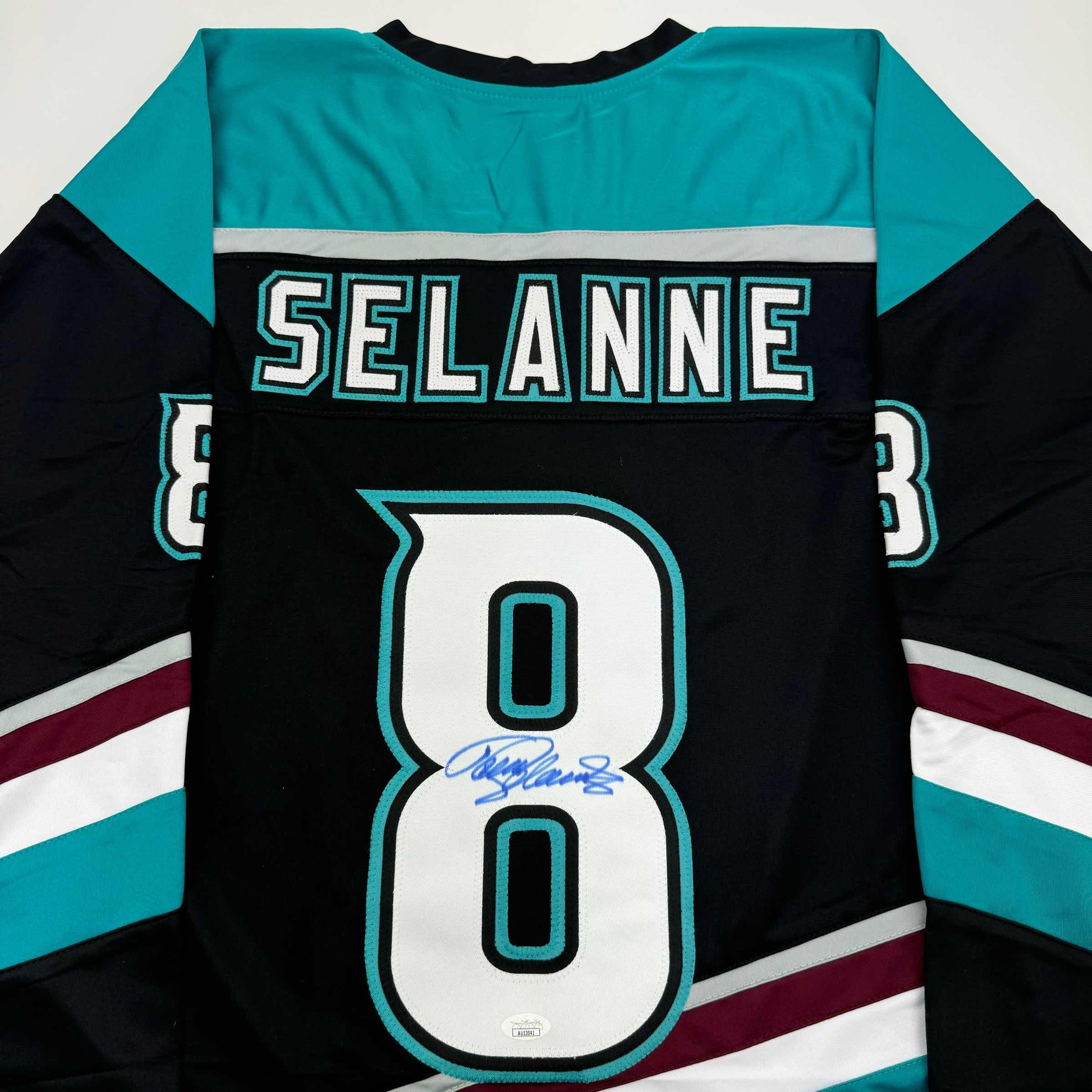 Back view of black hockey jersey with turquoise and white trim, displaying "SELANNE" and number 80 with blue autograph signature.