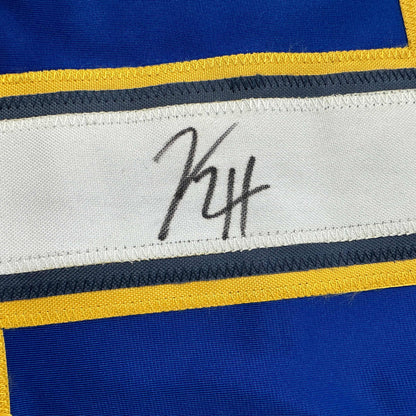 Close-up of autographed white stripe on blue and yellow hockey jersey showing handwritten signature "KH".