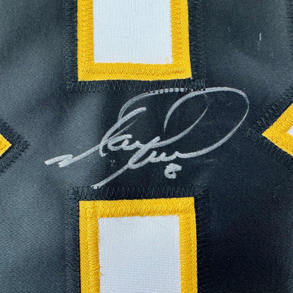 Close-up of autographed black hockey jersey with yellow and white trim showing handwritten signature in silver ink.