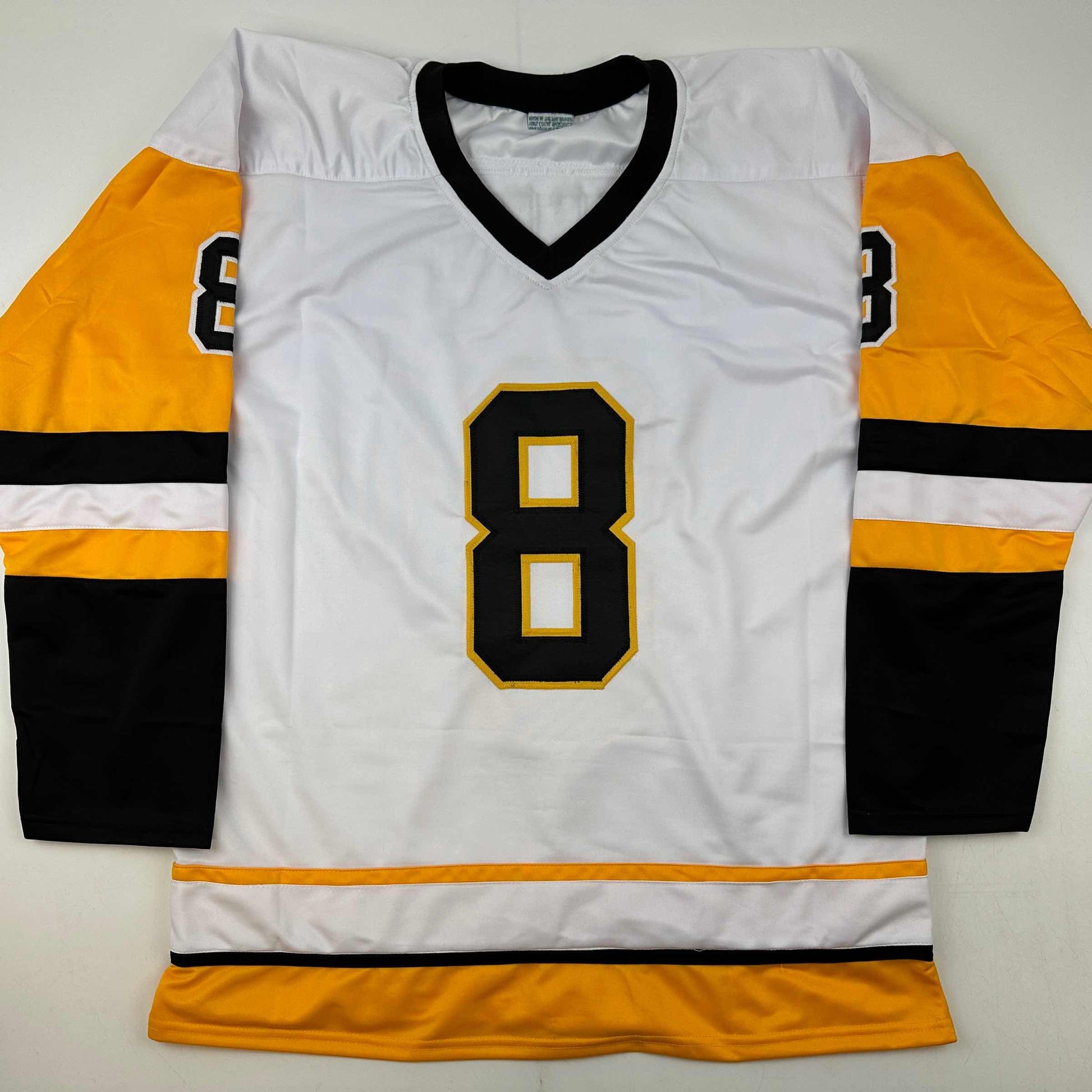 White hockey jersey with black and gold number 8, orange and black striped sleeves, displayed flat against white background.