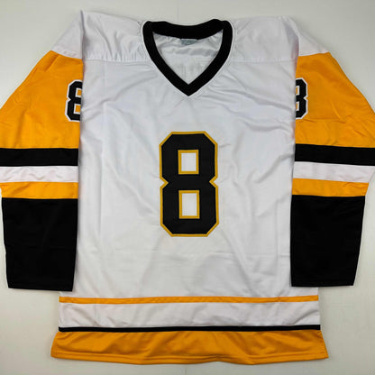 White hockey jersey with black and gold number 8, orange and black striped sleeves, displayed flat against white background.