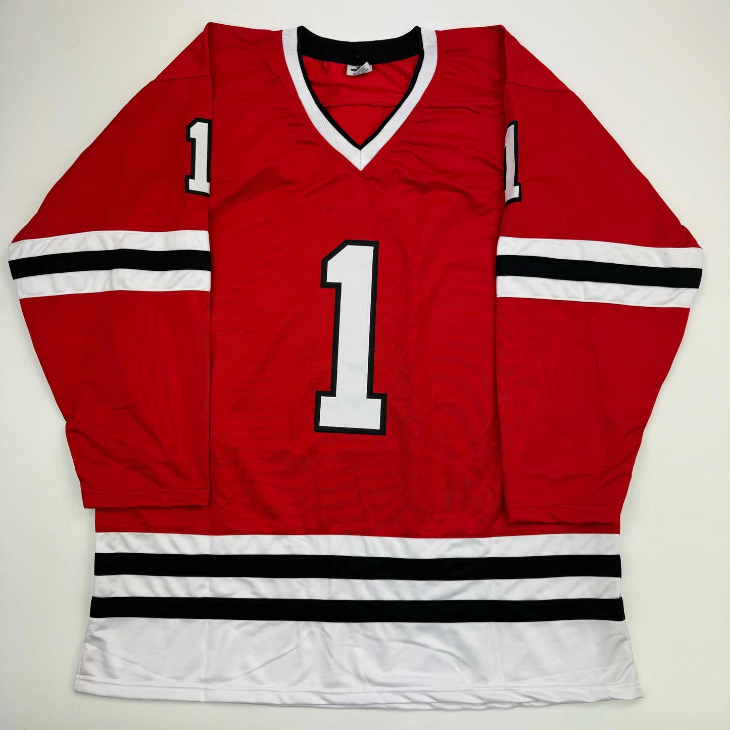 Red Chicago Blackhawks hockey jersey number 1 displayed flat against white background, showing front with V-neck collar and black-white striped sleeves.