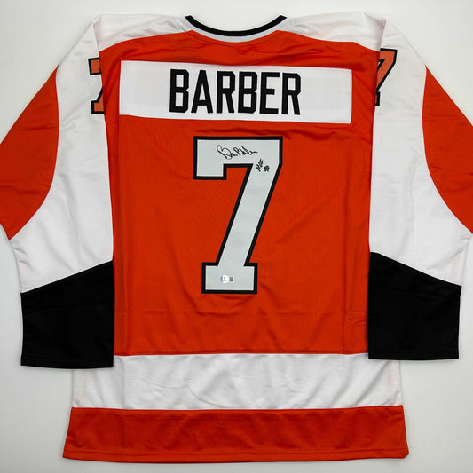 Back view of signed Bill Barber number 7 Philadelphia Flyers hockey jersey in red, white, and black with authentication sticker.