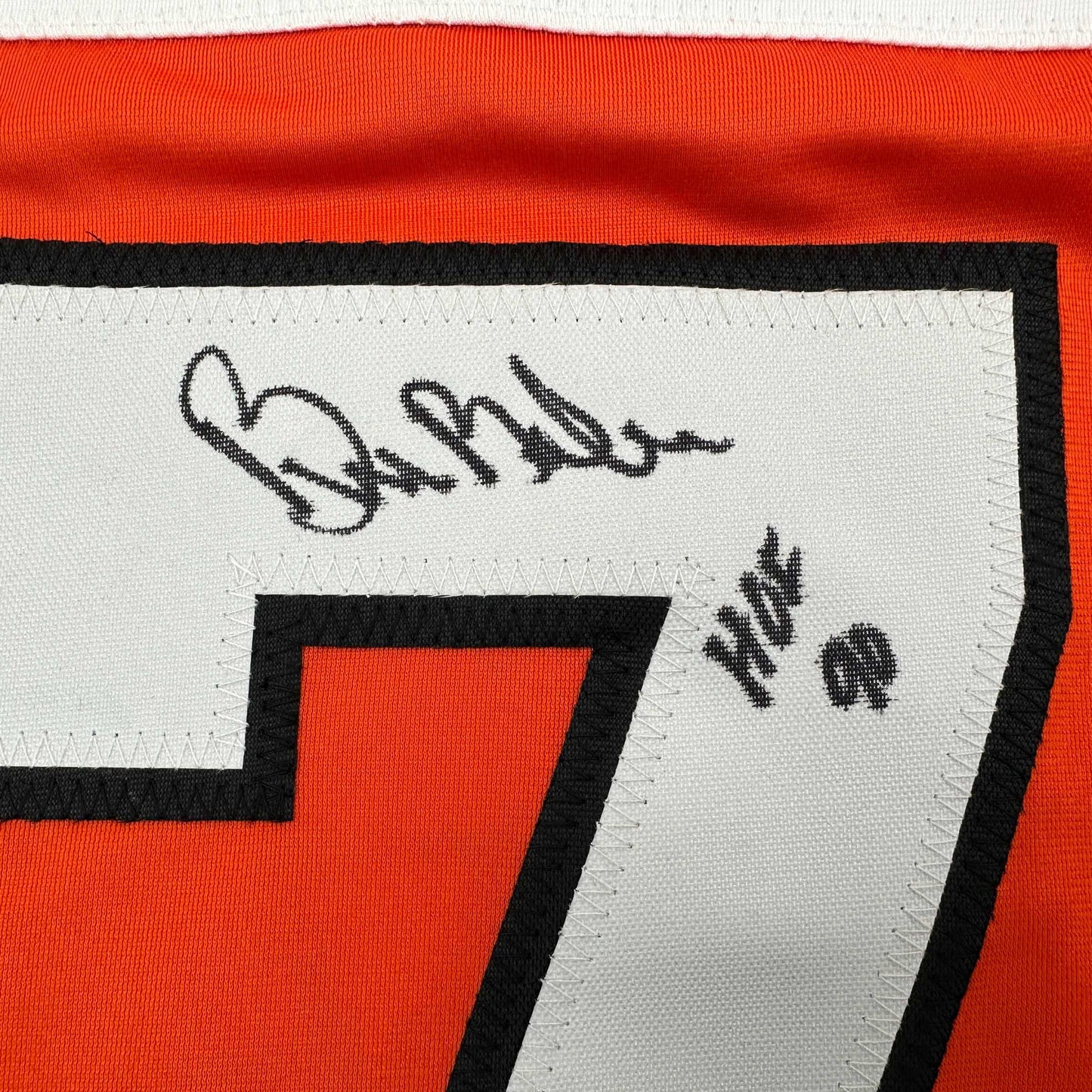 Close-up of signed orange and black Philadelphia Flyers hockey jersey showing autograph and "HOF 90" text on white label.