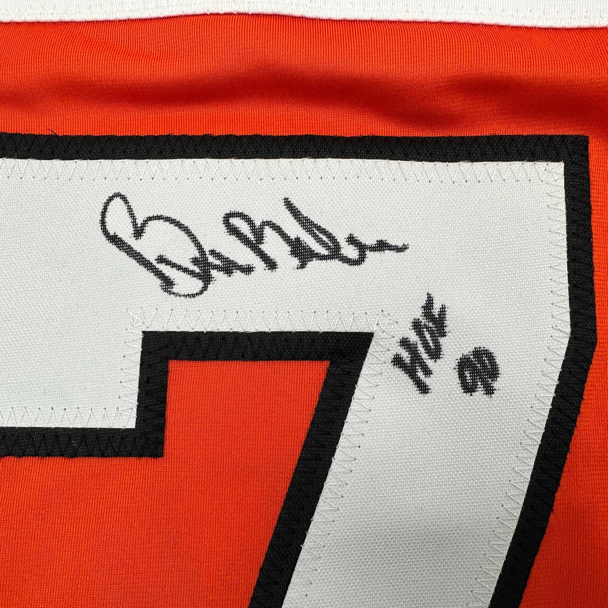 Close-up of signed orange and black Philadelphia Flyers hockey jersey showing autograph and "HOF 90" text on white label.