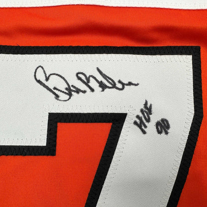 Close-up of signed orange and black Philadelphia Flyers hockey jersey showing autograph and "HOF 90" text on white label.