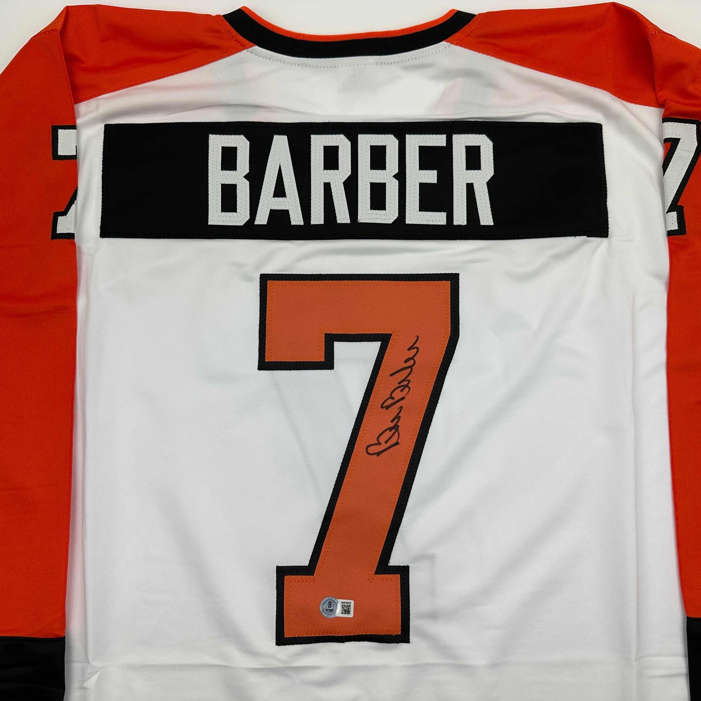 Back view of white hockey jersey with red sleeves showing "BARBER" nameplate and orange number 7 with signature.