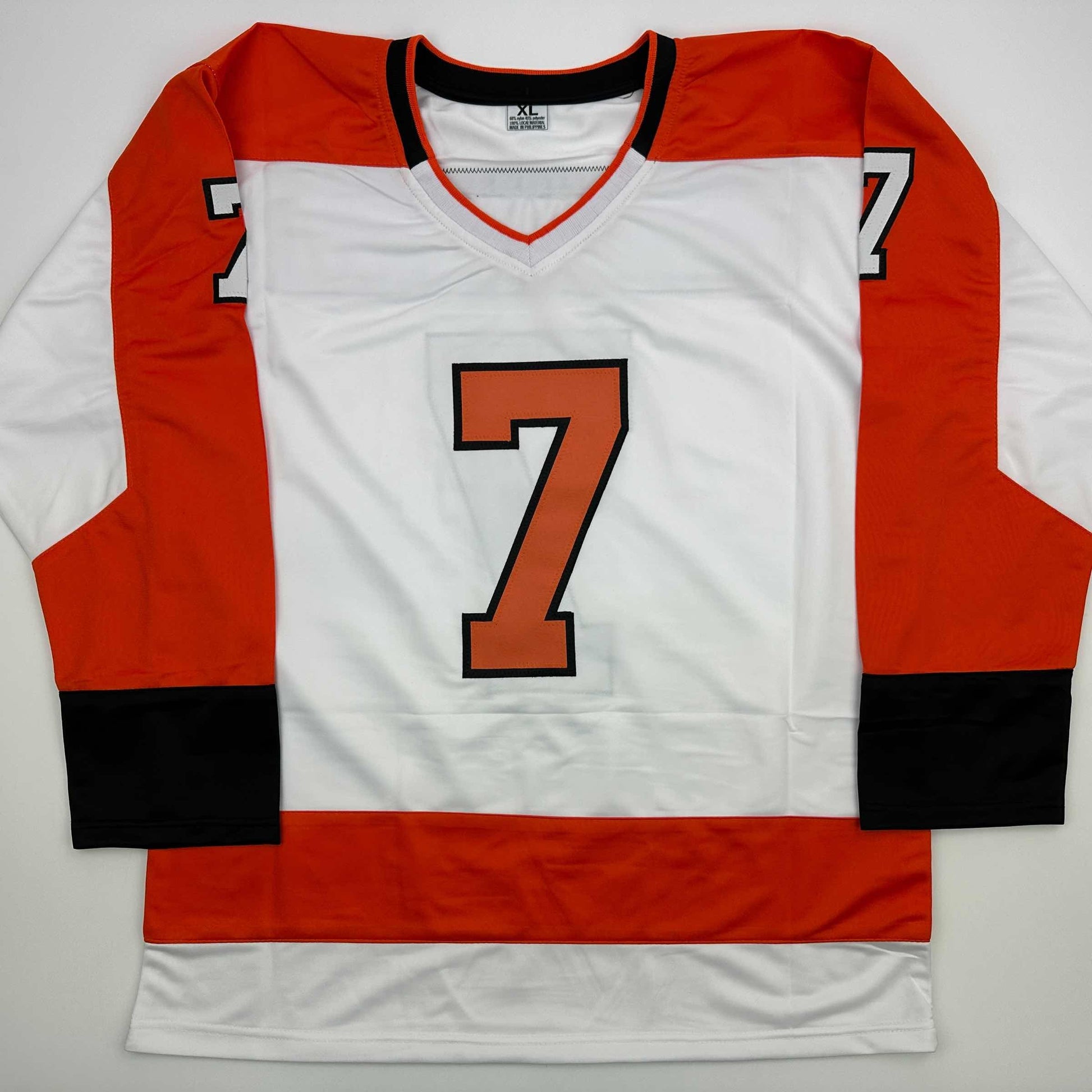 White Philadelphia Flyers hockey jersey with red and black sleeves displaying large orange number 7 on chest, flat lay front view.
