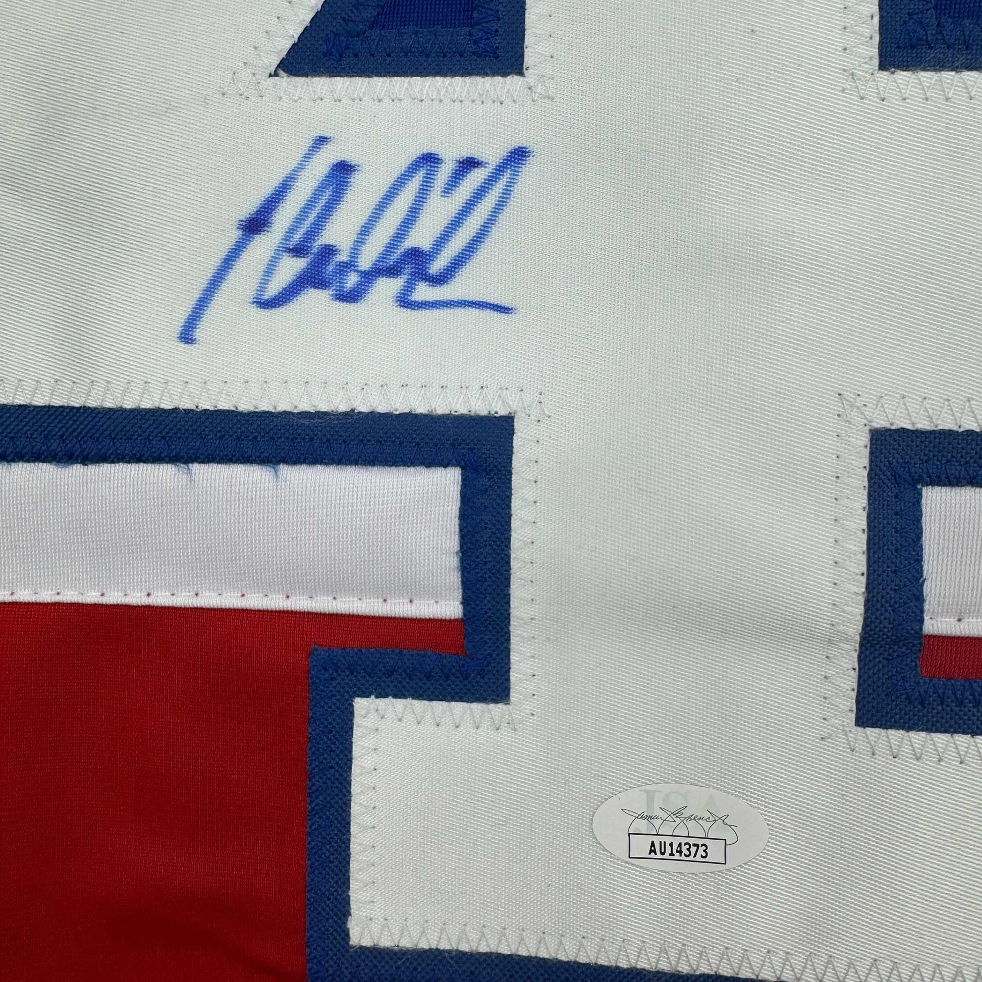 Close-up of blue autographed signature on white jersey fabric with red and navy striping and JSA authentication label visible.