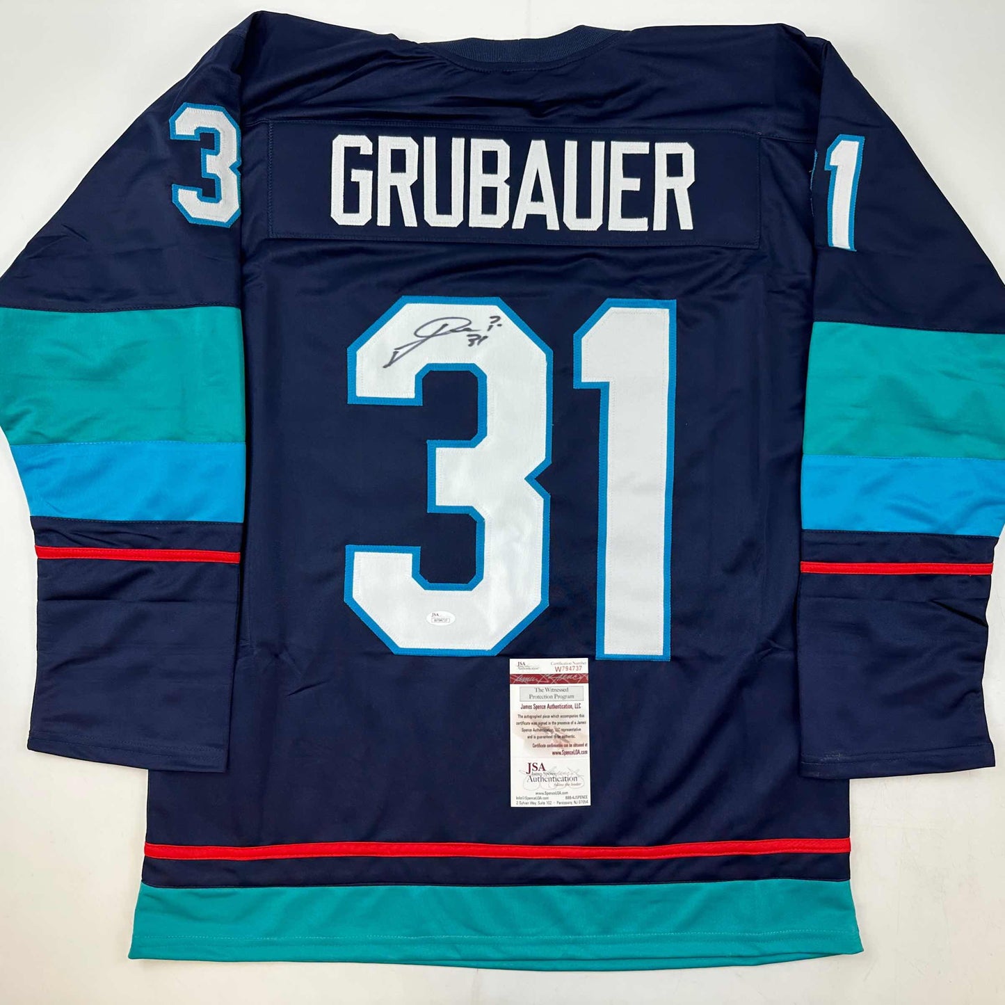 Reverse view of navy blue Seattle Kraken hockey jersey number 31 with "GRUBAUER" nameplate, teal and red stripes, JSA authentication label visible.