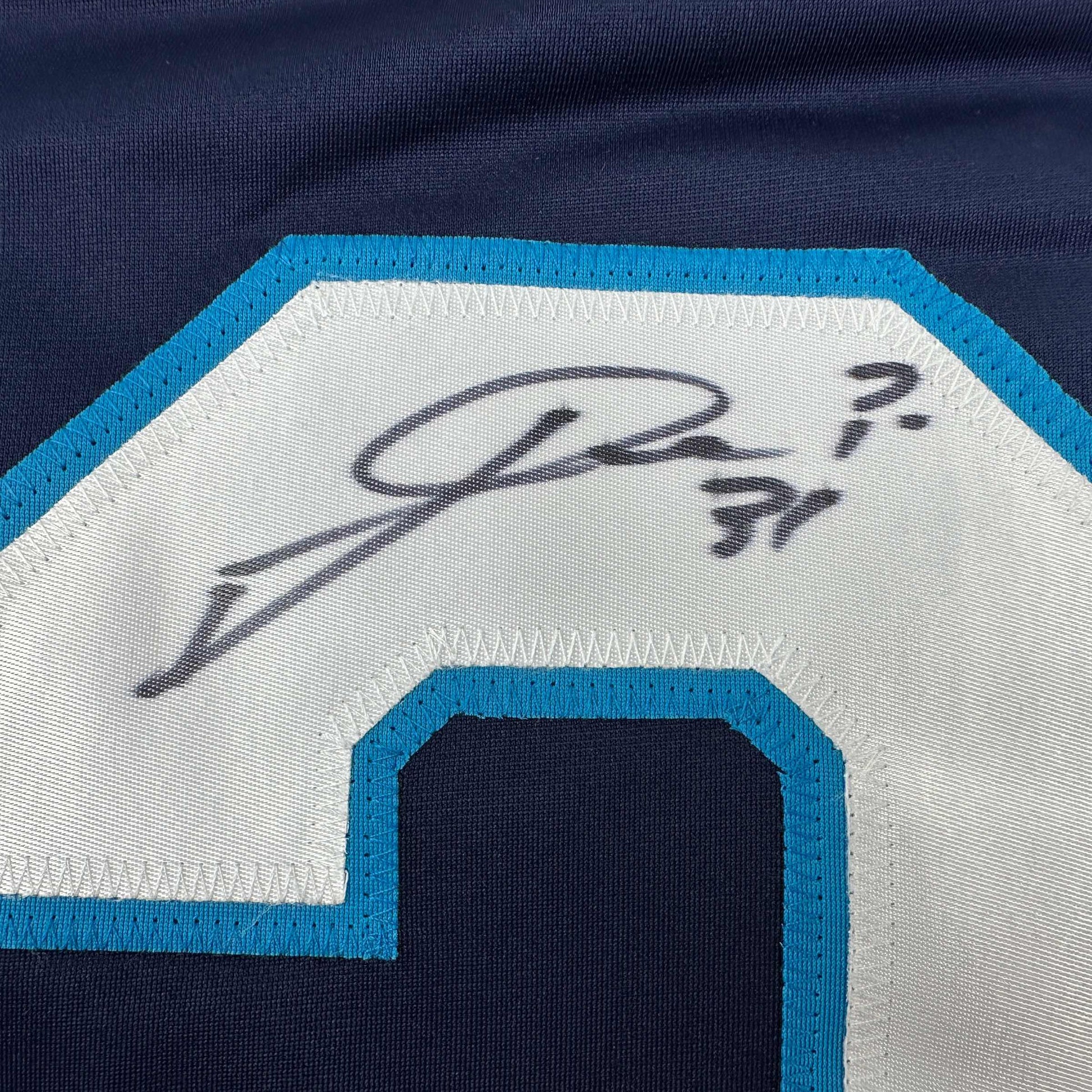 Close-up of embroidered signature on white fabric panel with blue trim of hockey jersey.
