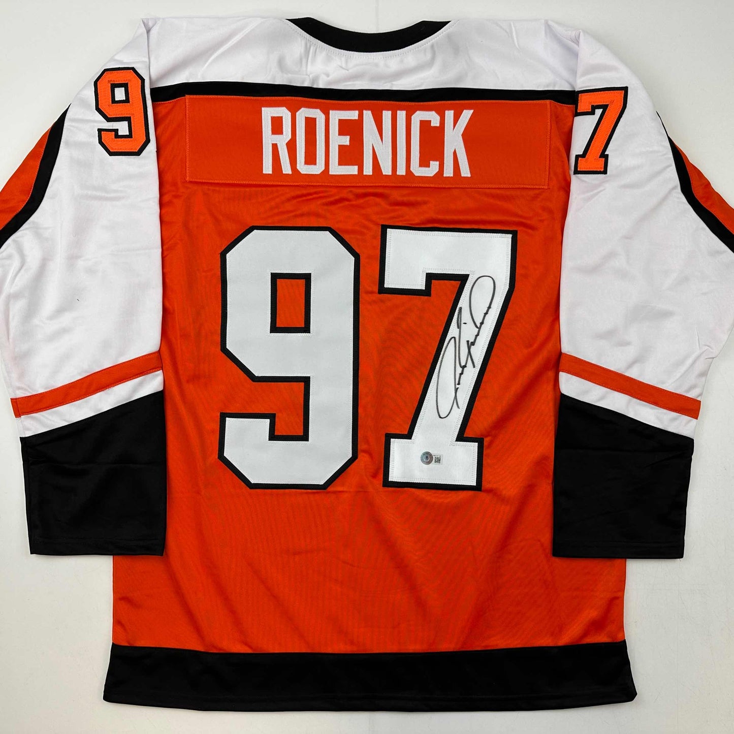 Back view of orange, white, and black hockey jersey with "ROENICK" and number 97 printed across shoulders, large white numbers on back, and autographed signature visible on lower right.