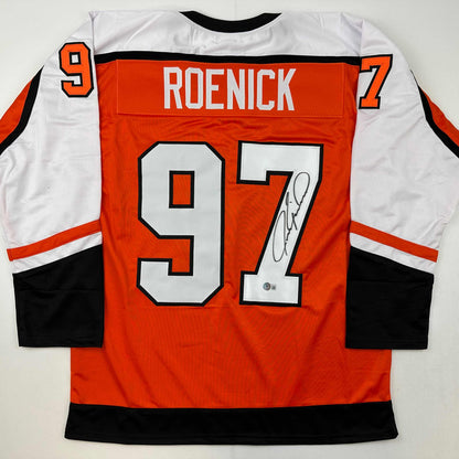 Back view of orange, white, and black hockey jersey with "ROENICK" and number 97 printed across shoulders, large white numbers on back, and autographed signature visible on lower right.