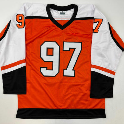 Orange hockey jersey with white and black trim, displaying large white numbers "97" on front and smaller numbers on shoulders, laid flat against white background.