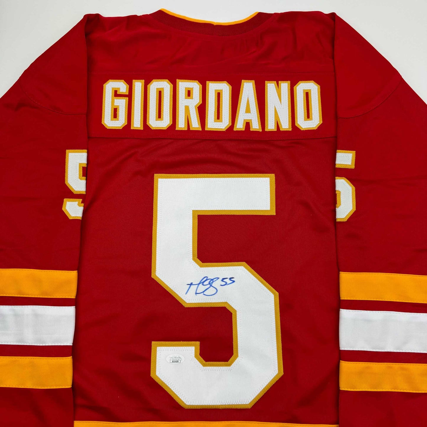Red Calgary Flames hockey jersey with "GIORDANO" and number 5 on back, autographed in blue ink.