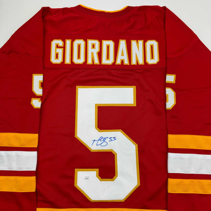 Red Calgary Flames hockey jersey with "GIORDANO" and number 5 on back, autographed in blue ink.