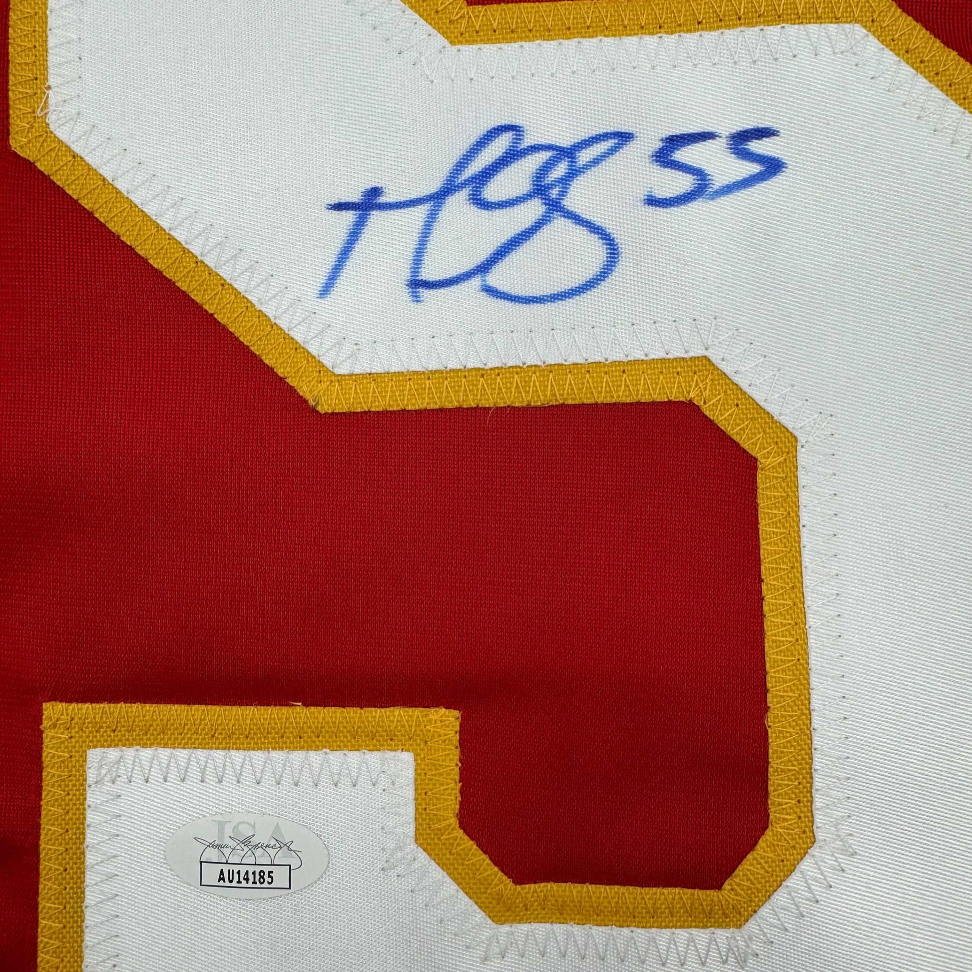 Close-up of signed red and gold hockey jersey with blue handwritten signature and JSA authentication sticker visible.