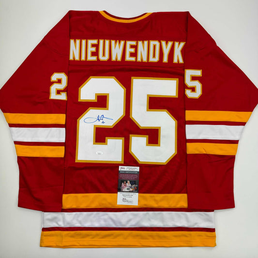 Red Calgary hockey jersey number 25 with "NIEUWENDYK" nameplate, signed in blue ink, displayed flat with JSA authentication label visible.