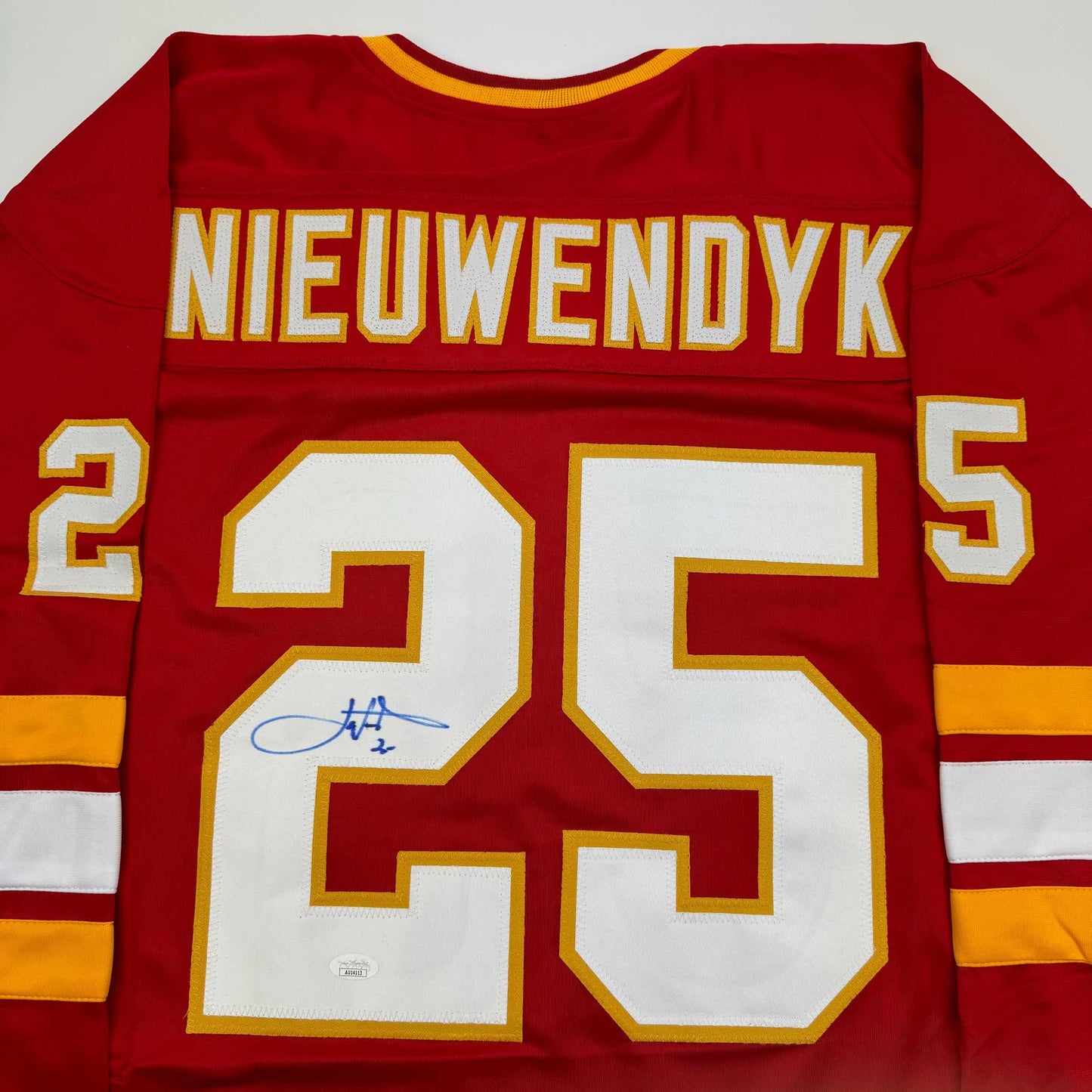 Red Calgary Flames hockey jersey displaying "NIEUWENDYK" and number 25 with blue autograph signature on white number.