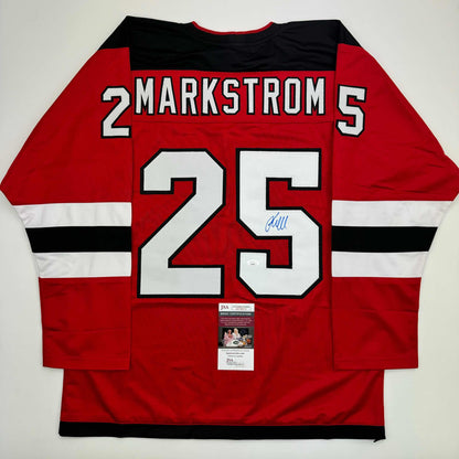 Red hockey jersey with white and black stripes displaying "MARKSTROM 25" and a JSA certification label, photographed flat lay from the back.