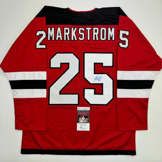 Red hockey jersey with white and black stripes displaying "MARKSTROM 25" and a JSA certification label, photographed flat lay from the back.
