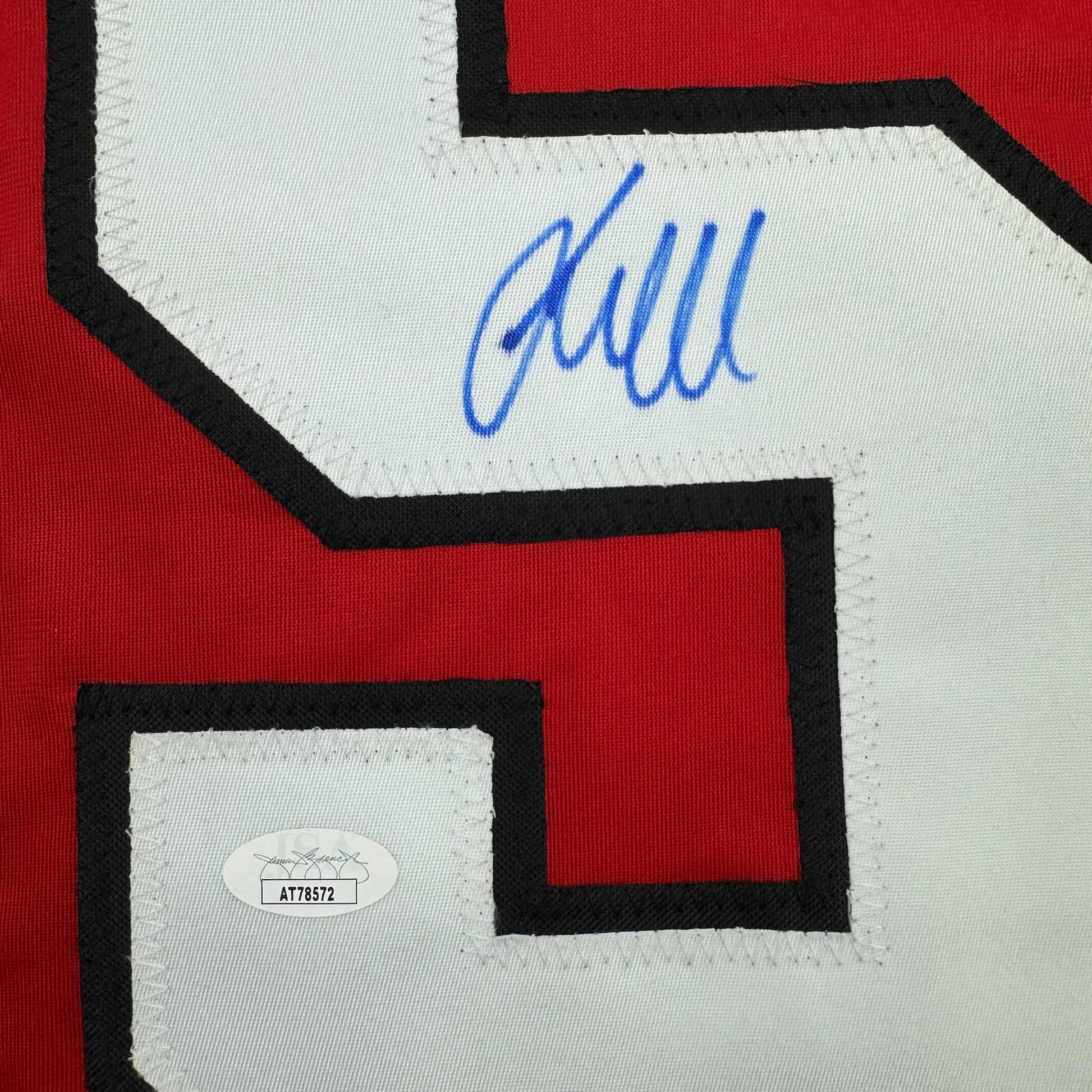 Close-up of blue autograph and JSA authentication sticker on red and white hockey jersey.