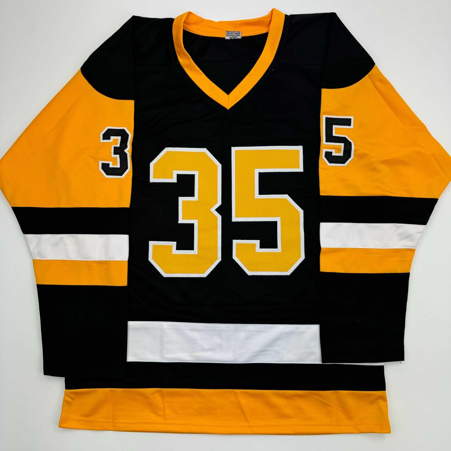 Black hockey jersey with gold and white number 35, orange sleeves, and gold V-neckline displayed flat against white background.